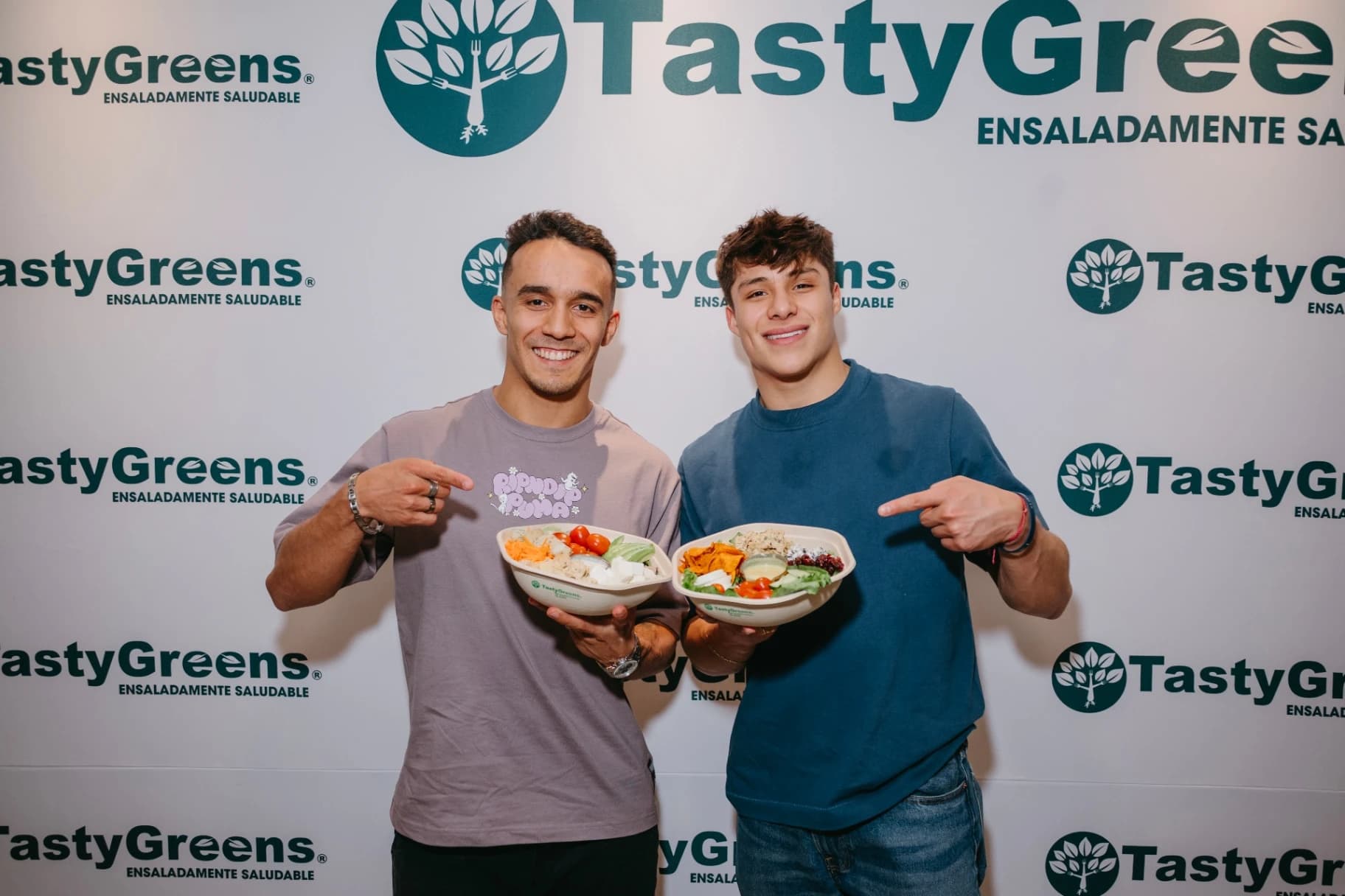 Osmar Olvera y Juan Manuel Celaya con ensaladas frente al backdrop Tasty Greens